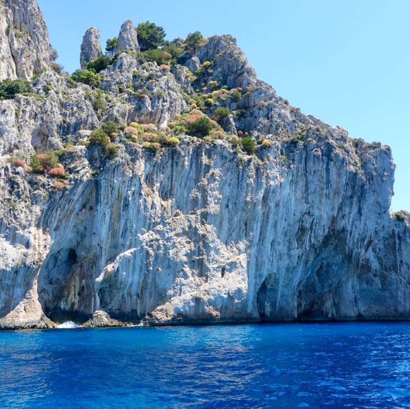 White limestone cliffs of Capri rising from deep blue sea near the Blue Grotto