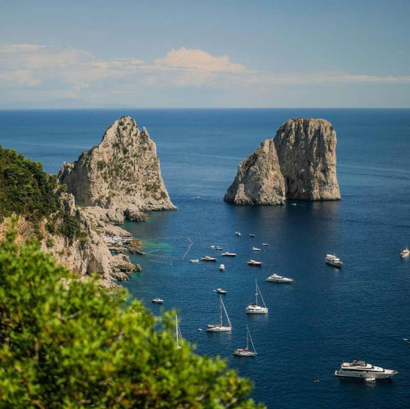 View of the Faraglioni rocks and anchored boats from the cliffs of Capri