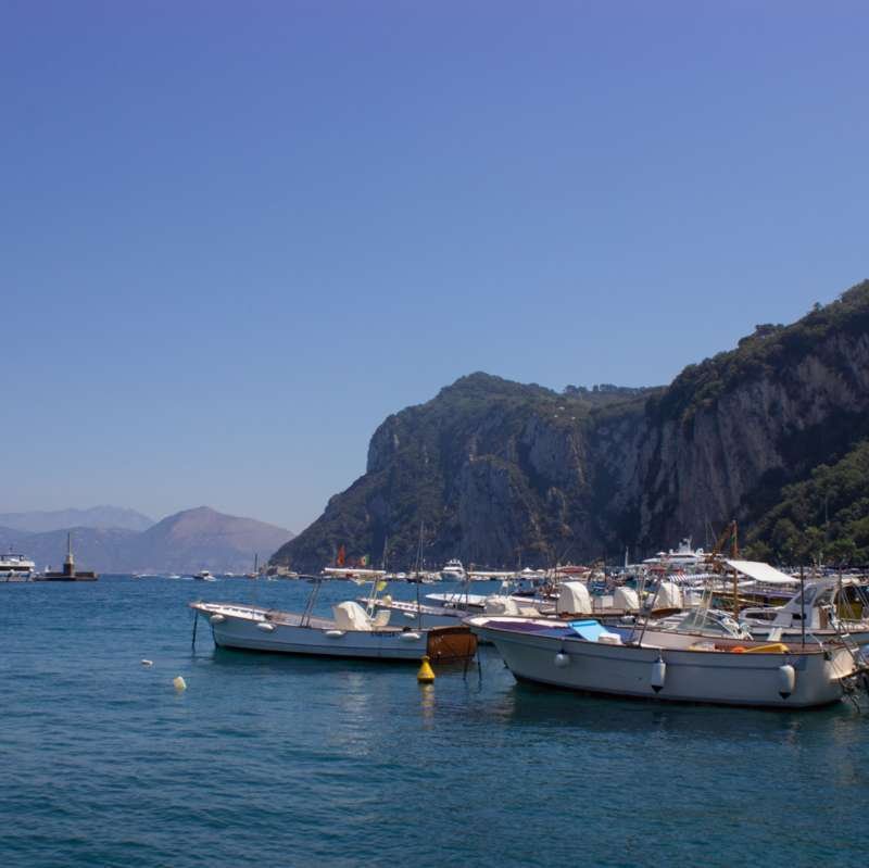 Fishing boats moored in Marina Grande harbor beneath the green cliffs of Capri