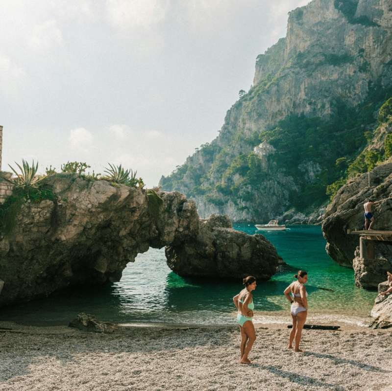 Bathers on the pebble beach of Marina Piccola on Capri with rock arch and green cliffs
